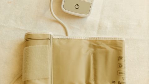 Top view of a digital blood pressure monitor and cuff on white fabric background.