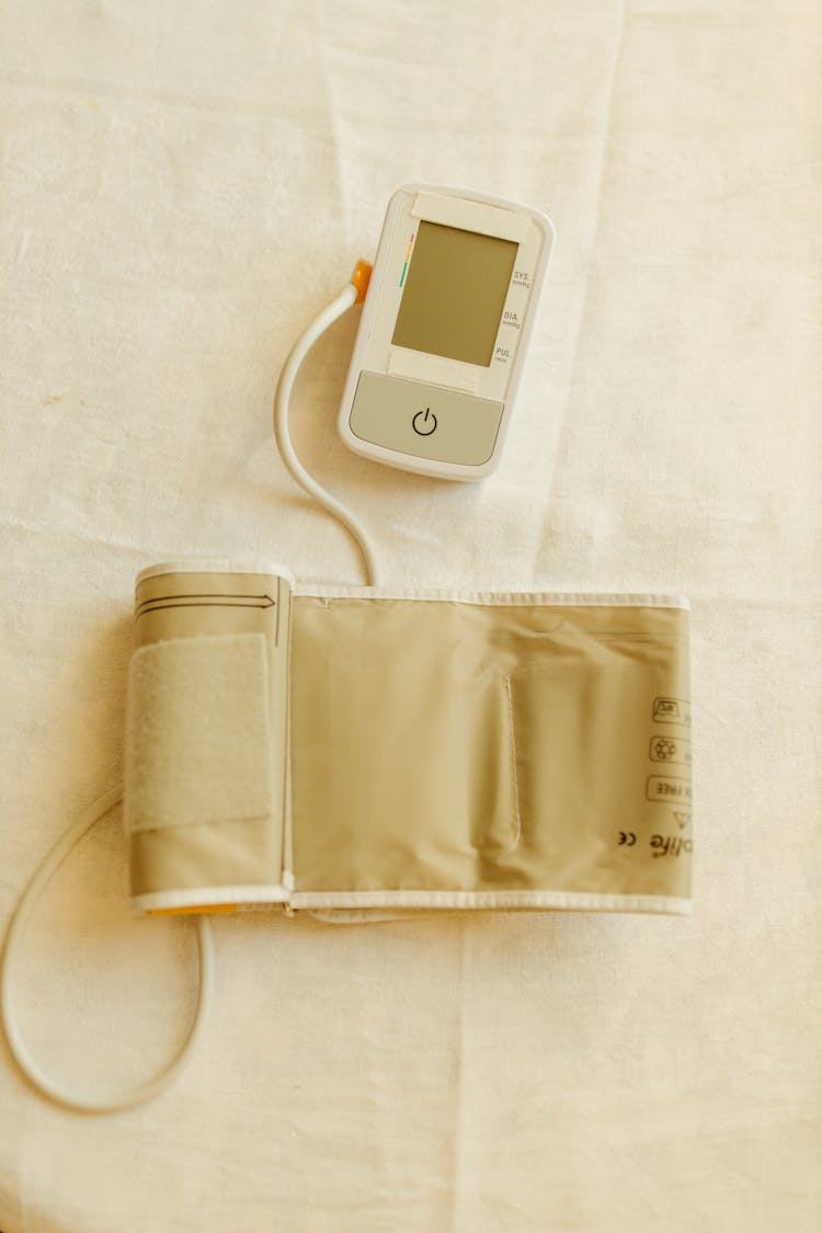 Digital Blood Pressure Monitor And Pressure Cuff On White Fabric 