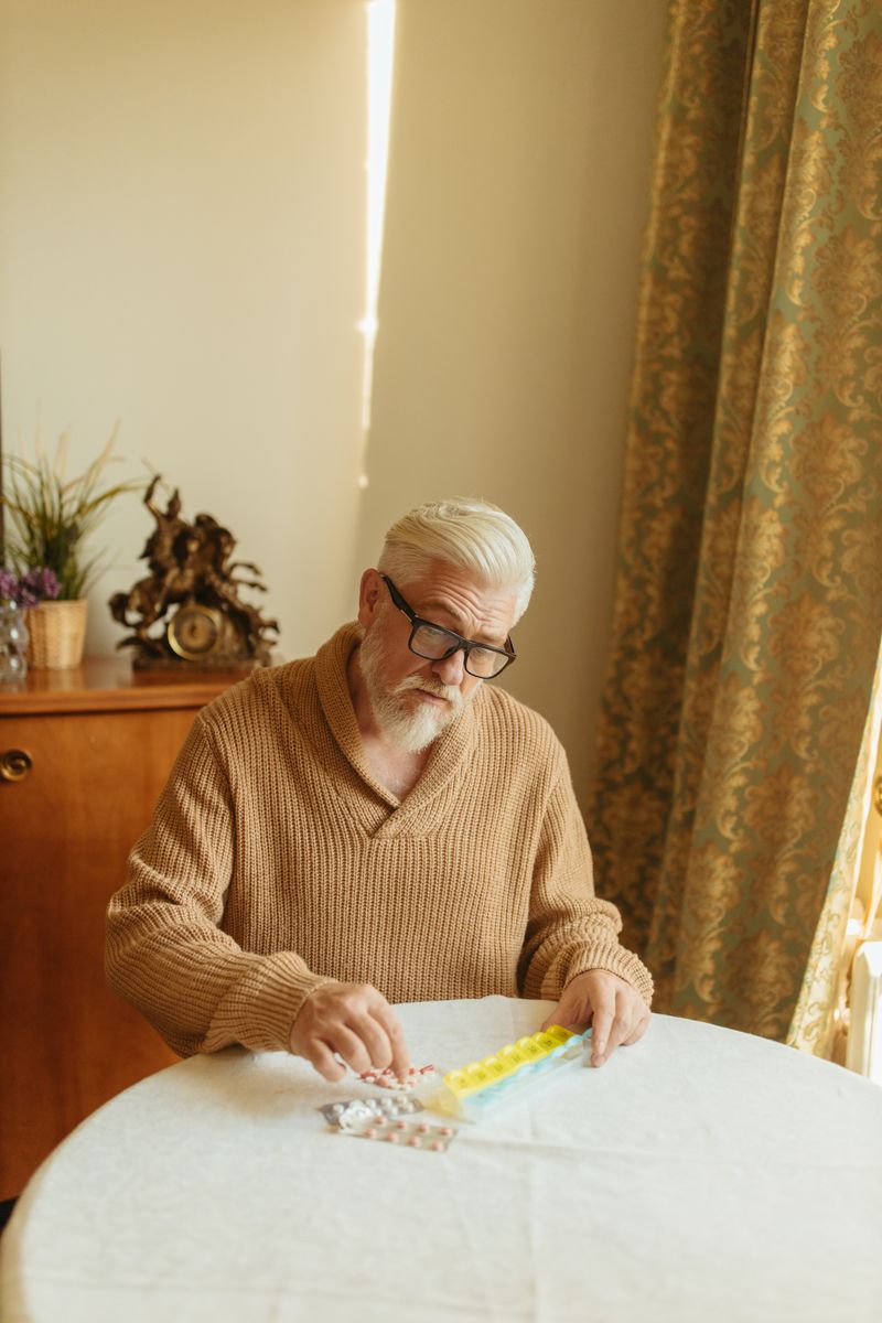 An older man sorting tablets into a daily pill organiser at a table