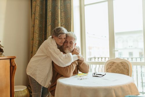 Free A loving elderly couple shares a warm embrace at a dining table indoors, symbolizing affection and togetherness. Stock Photo
