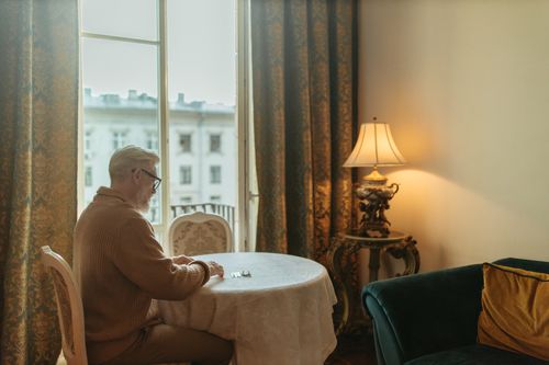 Free A senior man with white hair sits by a table in a vintage room. Stock Photo