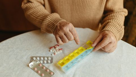Senior adult organizing daily medications using a weekly pill organizer on a table indoors.