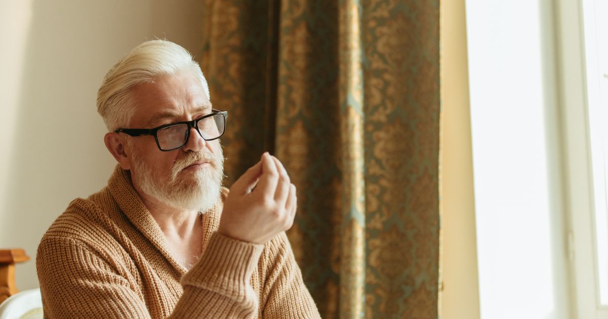 Senior man with glasses sitting thoughtfully at a table with a weekly pill organizer