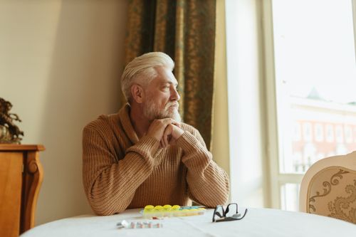 Free Elderly man with a beard sitting by a window, looking thoughtful. Stock Photo