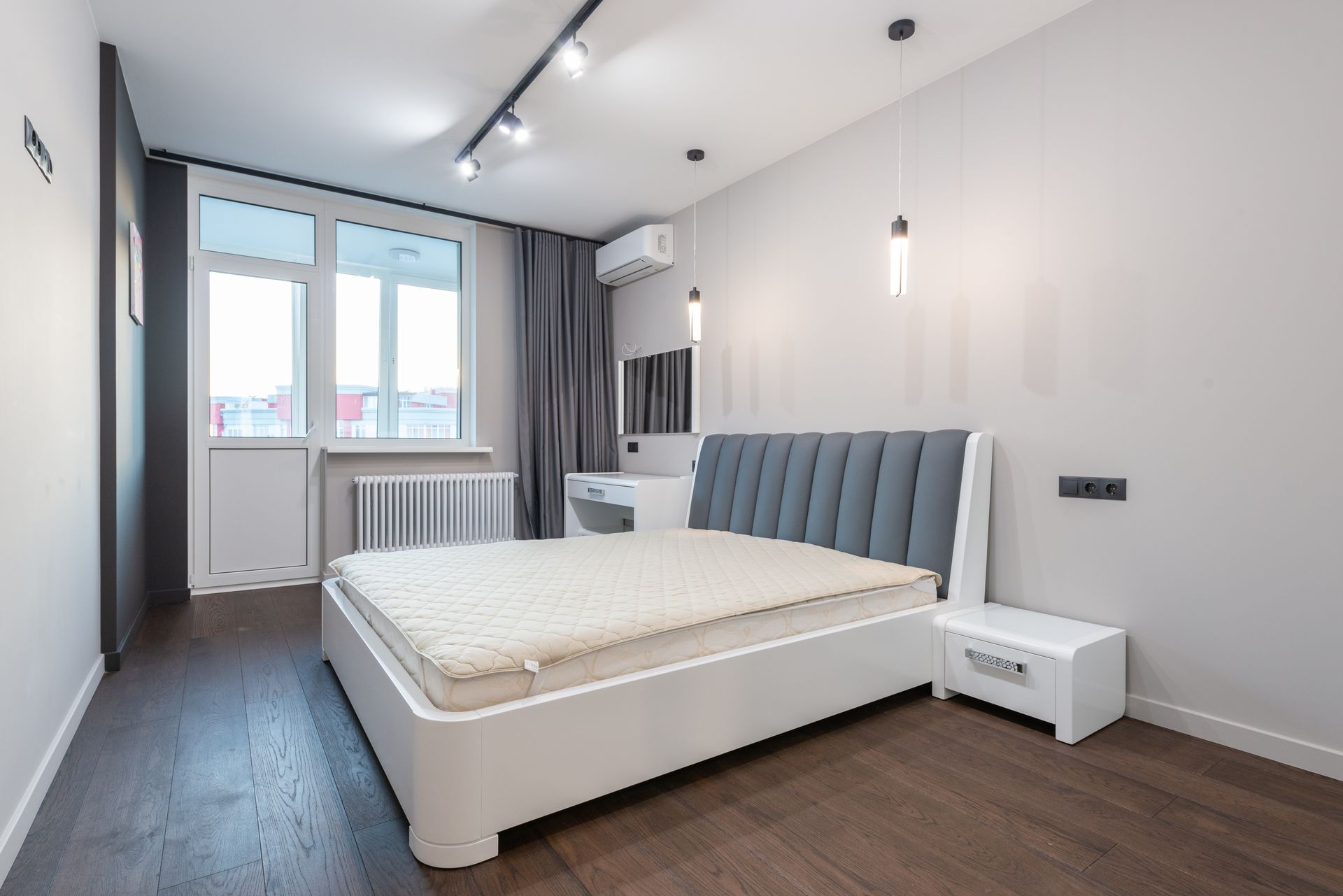 Spacious minimalist bedroom featuring modern design elements with white walls and parquet flooring.