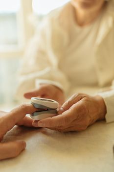 Elderly person checks pulse with a finger pulse oximeter in a bright room.