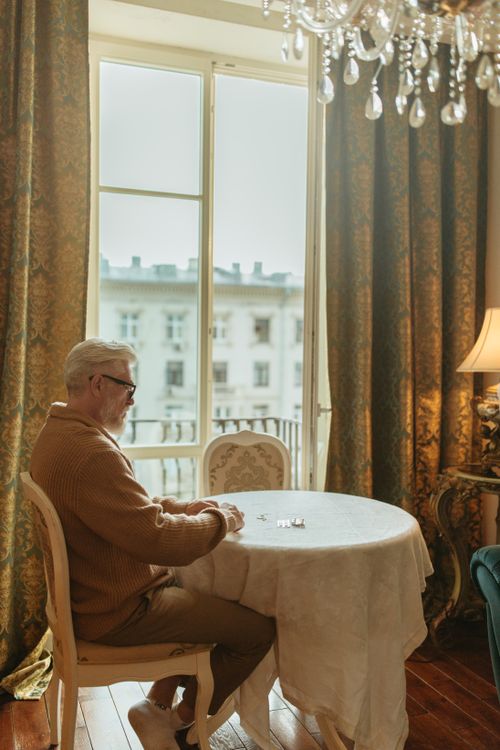 Free Senior man in brown sweater sitting near window in a cozy room. Stock Photo