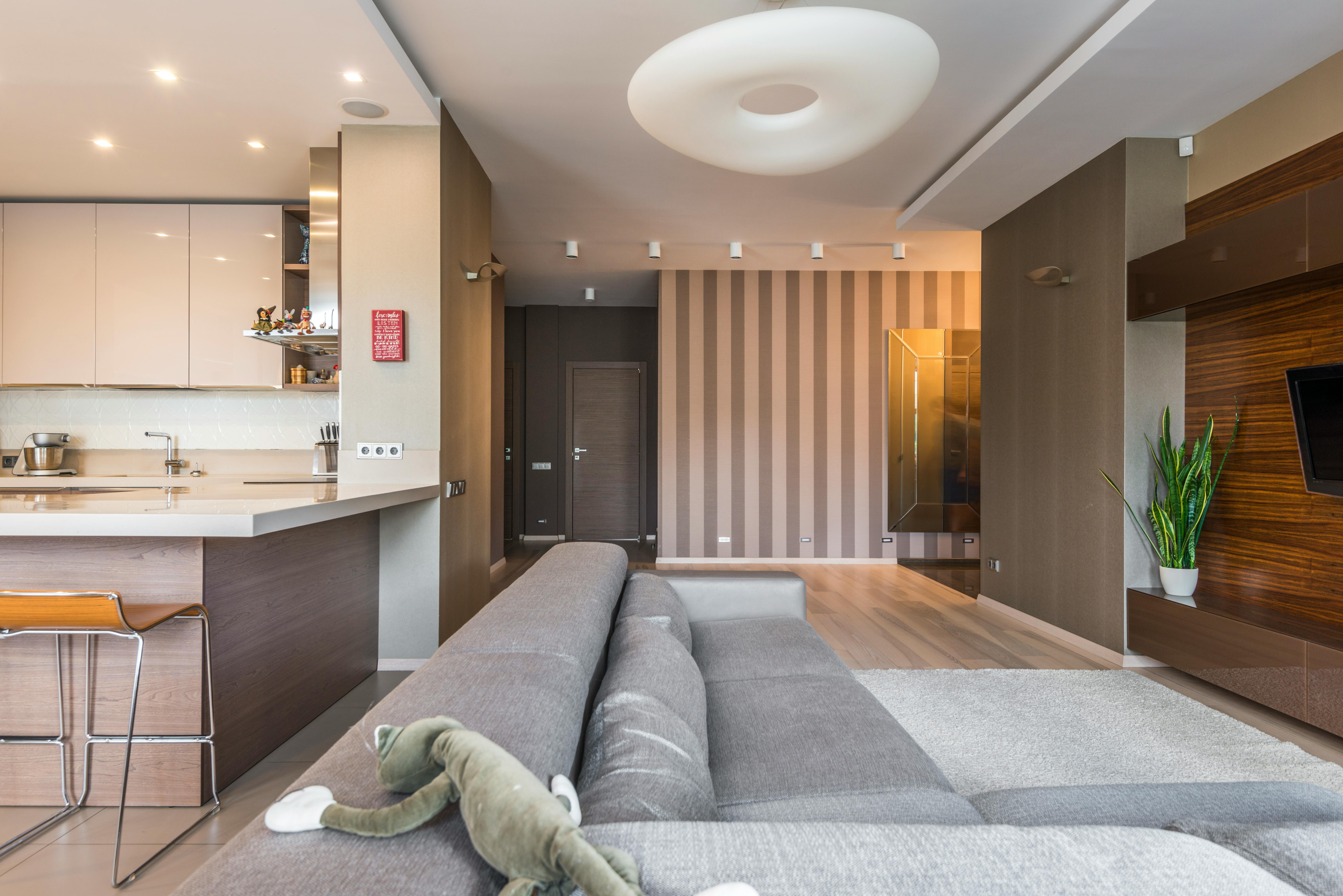 Nowoczesny salon z aneksem i szarym tapczanem ustawionym plecami do kuchni