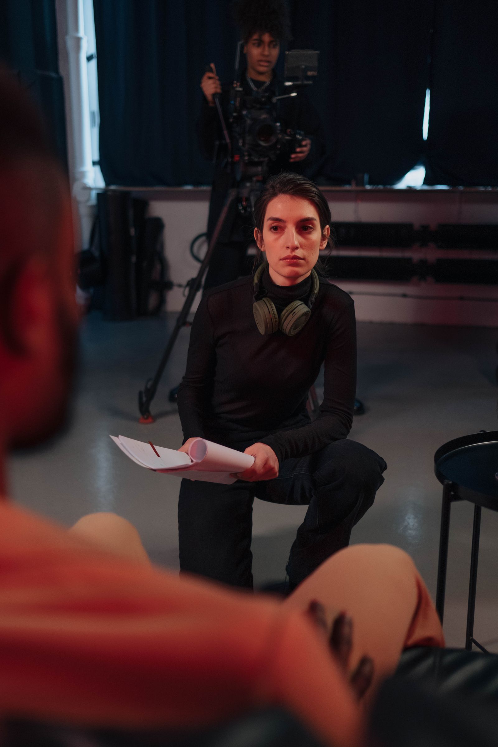 A director with a script and headphones crouched on set while a camera operator films behind her