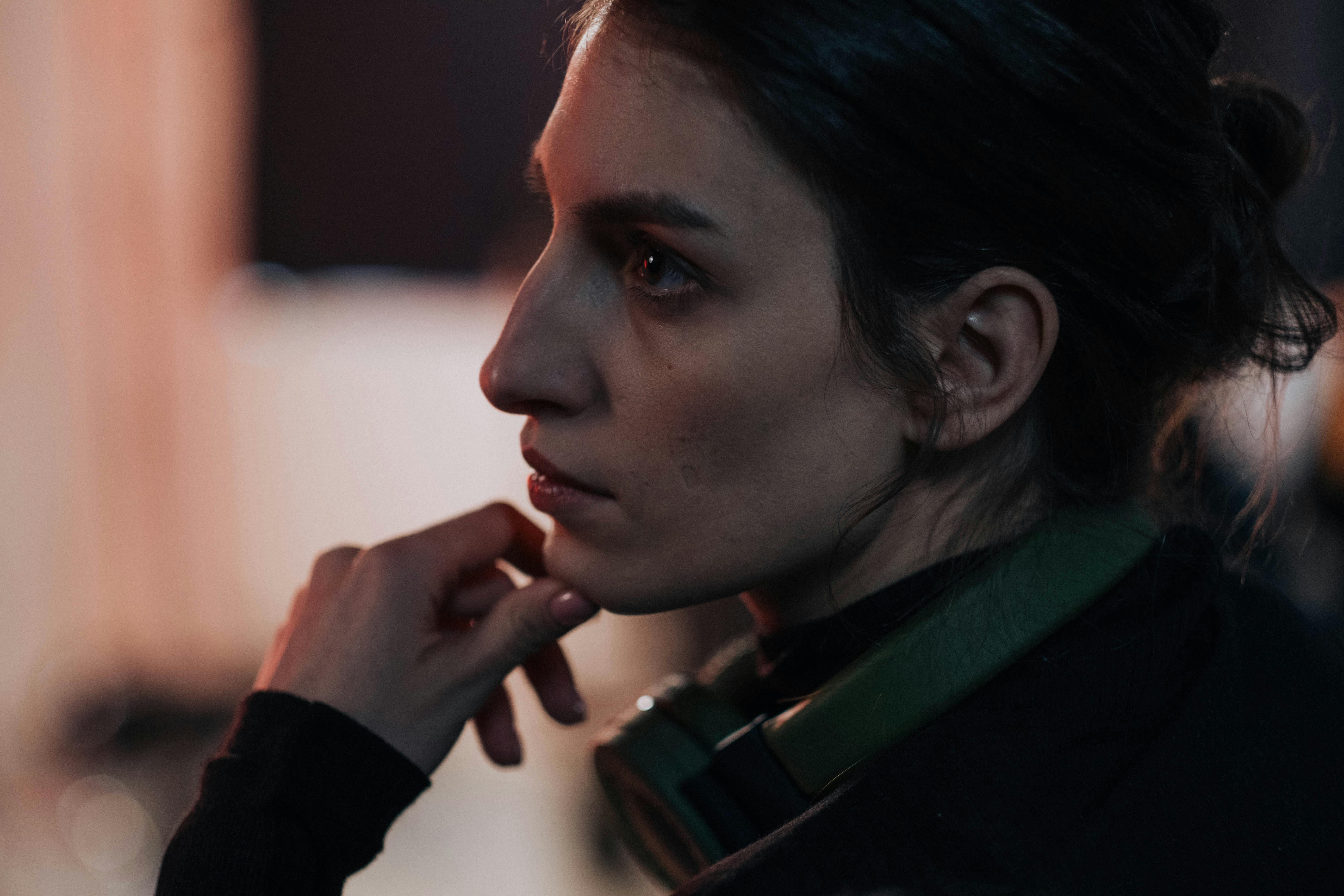 Side profile of a thoughtful woman with headphones in a dimly lit studio.