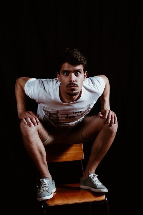 Man Wearing White Crew-neck Short-sleeved Shirt Sitting on Brown Wooden Chair