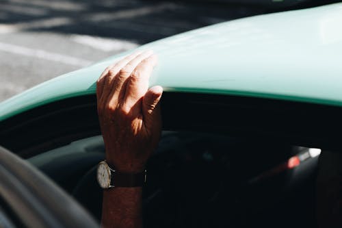 бесплатная Человек, носящий круглые белые аналоговые часы с черным ремешком, держится на крыше автомобиля Стоковое фото
