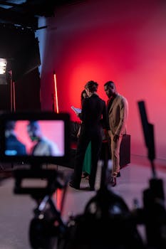 Film set with actors and crew in a studio with vibrant red lighting.