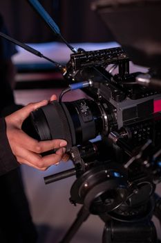 Close-up of hands adjusting a professional video camera lens during a shoot, showcasing studio equipment.