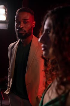 Two people on set under dramatic colored lighting, showcasing intense expressions.