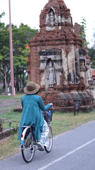 A woman rides her bicycle past historic brick ruins under a clear blue sky, embracing a serene journey.