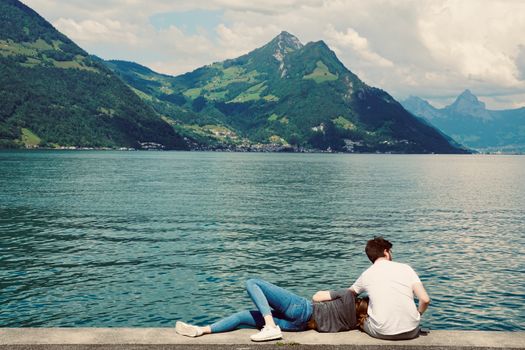 A couple enjoys a relaxing moment by a picturesque mountain lake, surrounded by lush scenery.