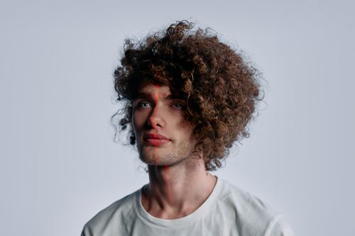 Free Portrait of a young man with curls and futuristic laser patterns on a plain white background. Stock Photo