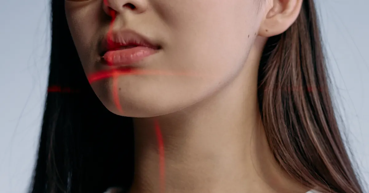 A close-up of a woman's lips, chin and neck with thin red laser lines across her skin, representing consent for using a real person's face and voice in AI content