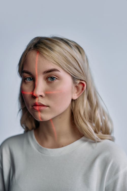 Free A woman with laser lines on her face highlighting facial recognition technology, set against a plain white background. Stock Photo