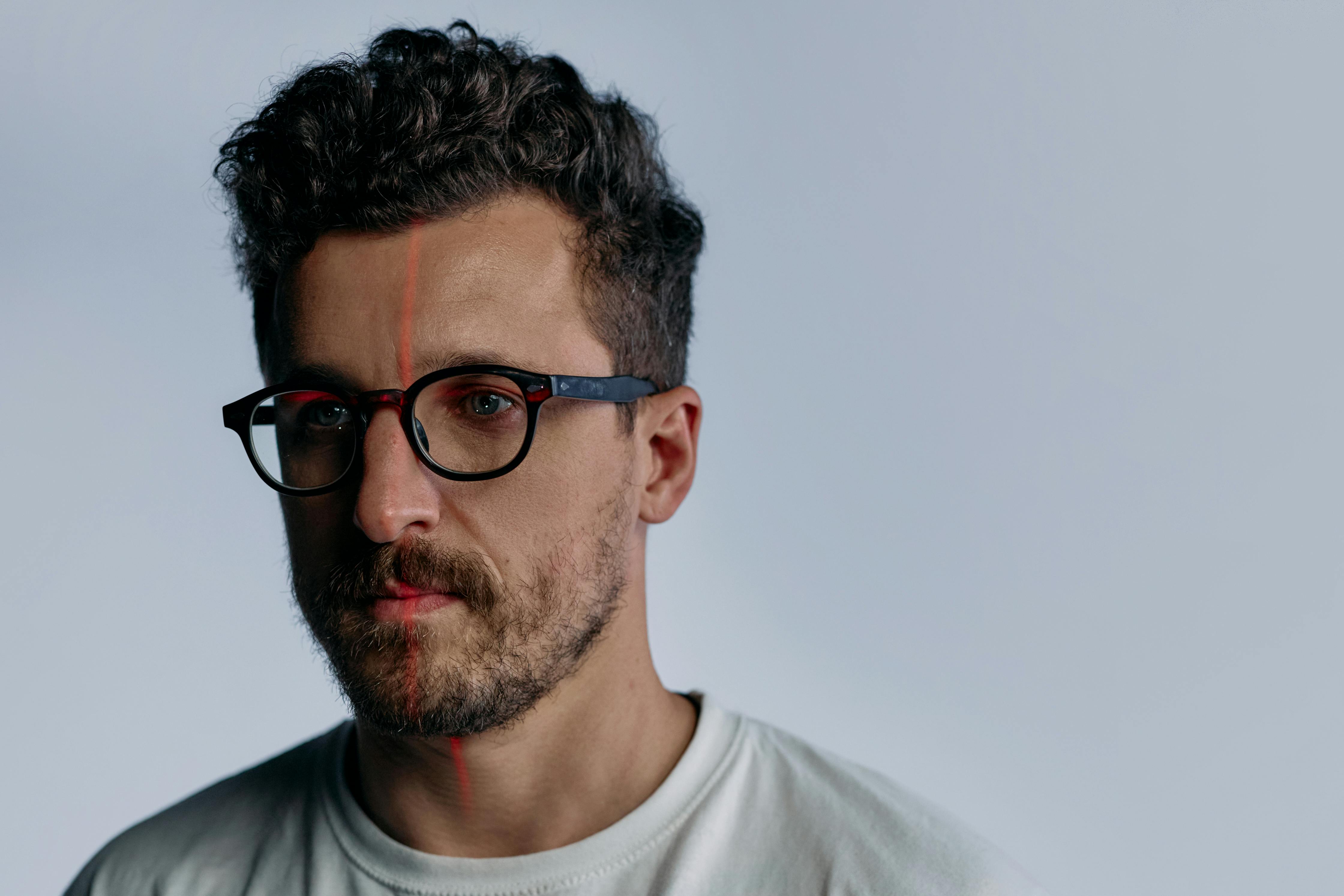 A Man Wearing Black Framed Eyeglasses with Red Laser Light Reflected on