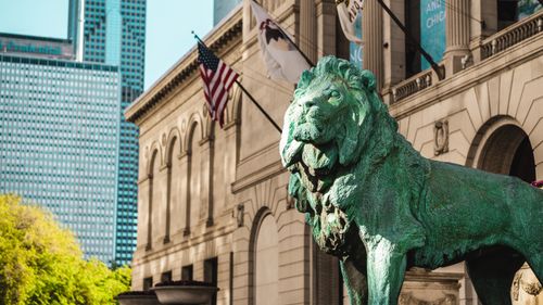 Free A striking bronze lion statue outside the Art Institute of Chicago with flags in the background. Stock Photo