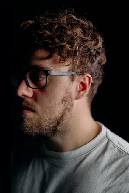 Studio portrait of a man with glasses and beard against black background.