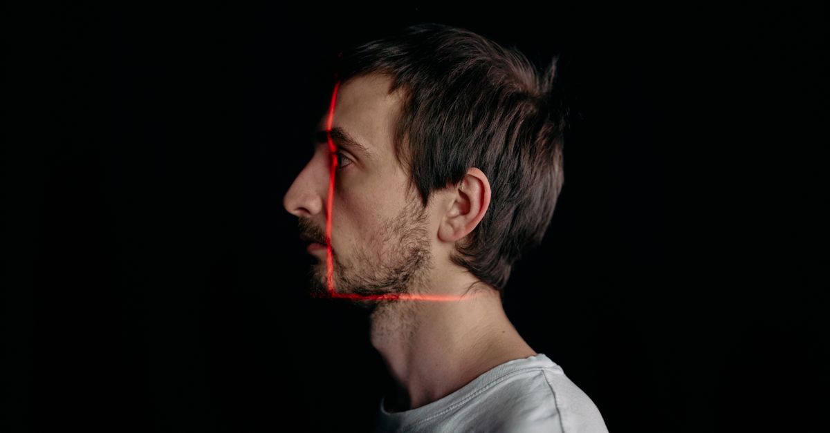 Side profile of a man with red scanning lines projected across his face against black
