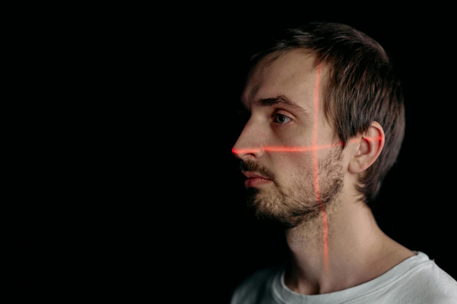 A side profile of a man with facial recognition laser scan on his face against a black background.