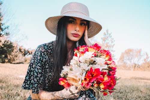 Woman In Floral Dress With Sun Hat Holding A Bunch of Flowers