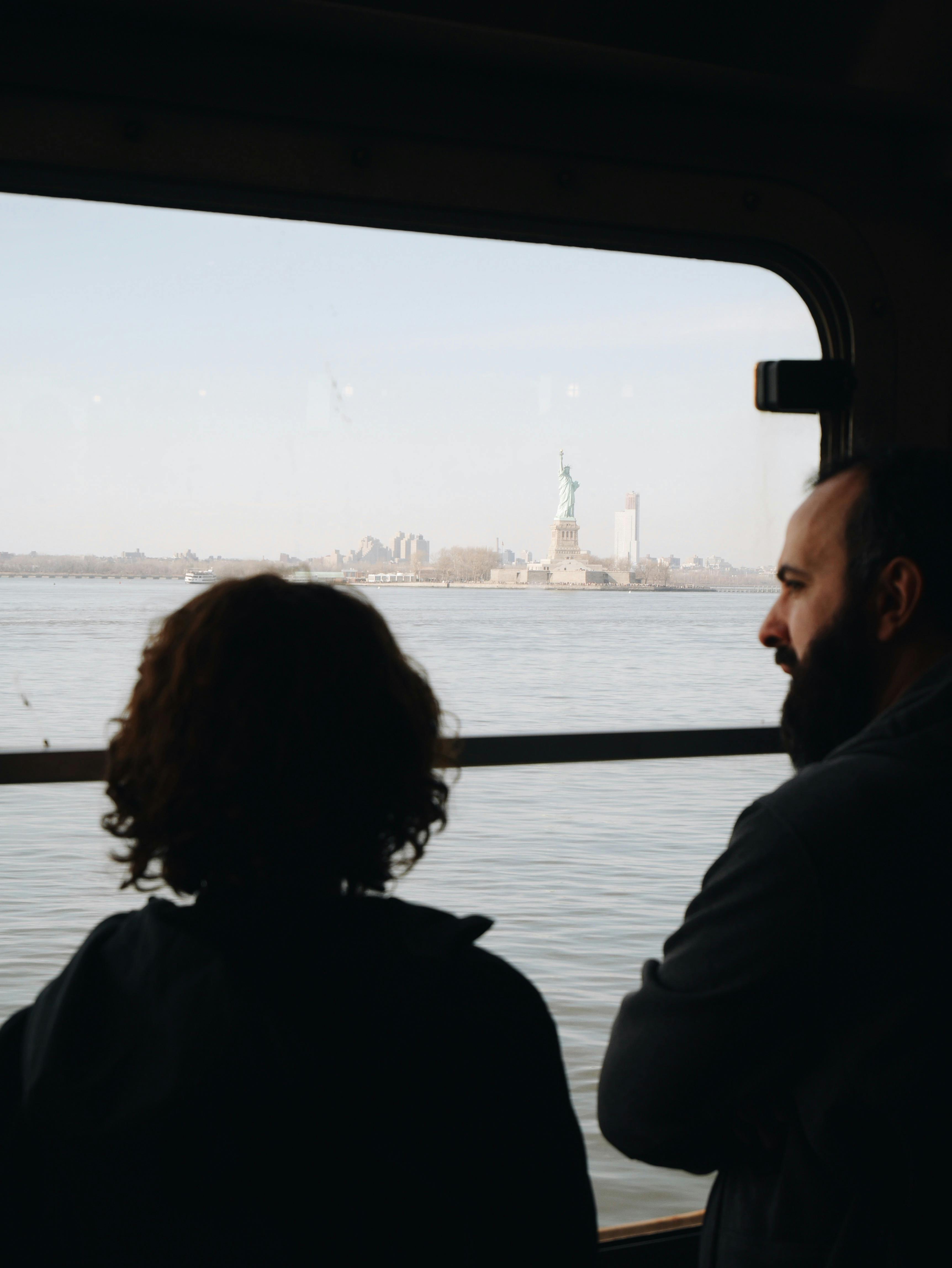 Passengers on a ferry admire the Statue of Liberty on a clear day from the boat window.