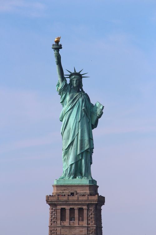 Free Iconic Statue of Liberty under a blue sky in New York City, a must-see attraction. Stock Photo