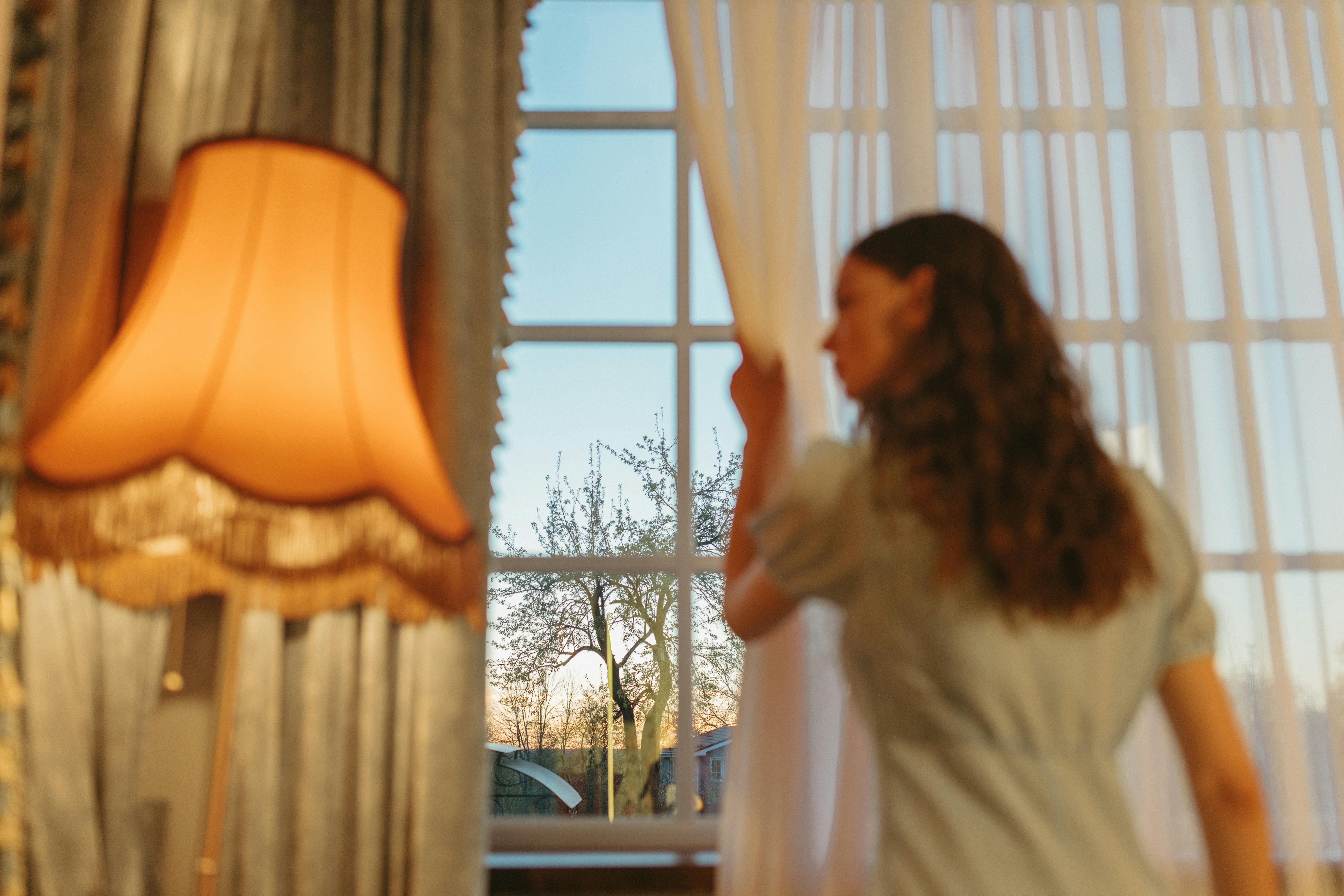 Woman opening clean white sheer curtains in a bright Dubai home