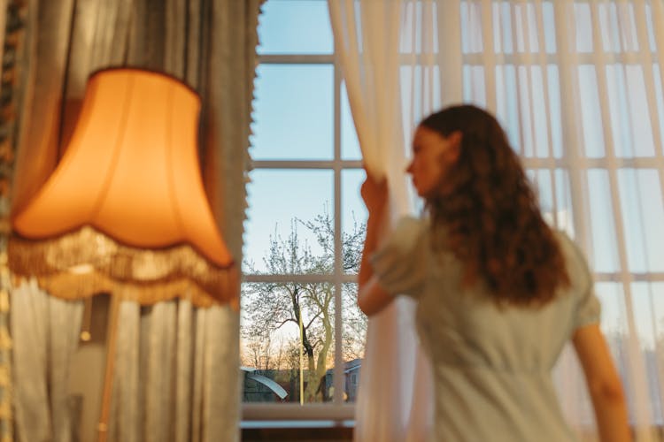 A Person Drawing The Window Curtain