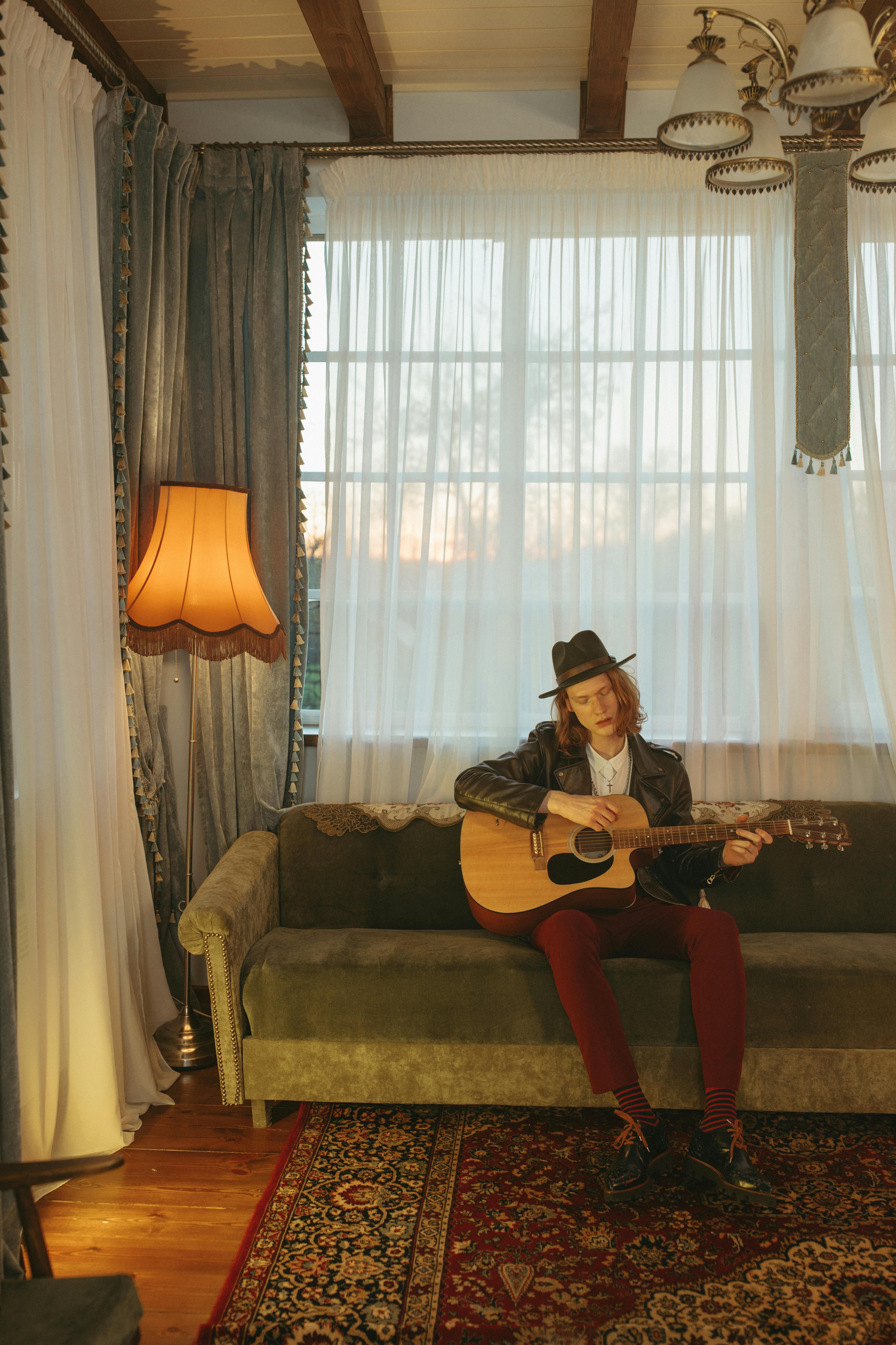 Young man playing acoustic guitar on a sofa, enjoying serene indoor ambiance.