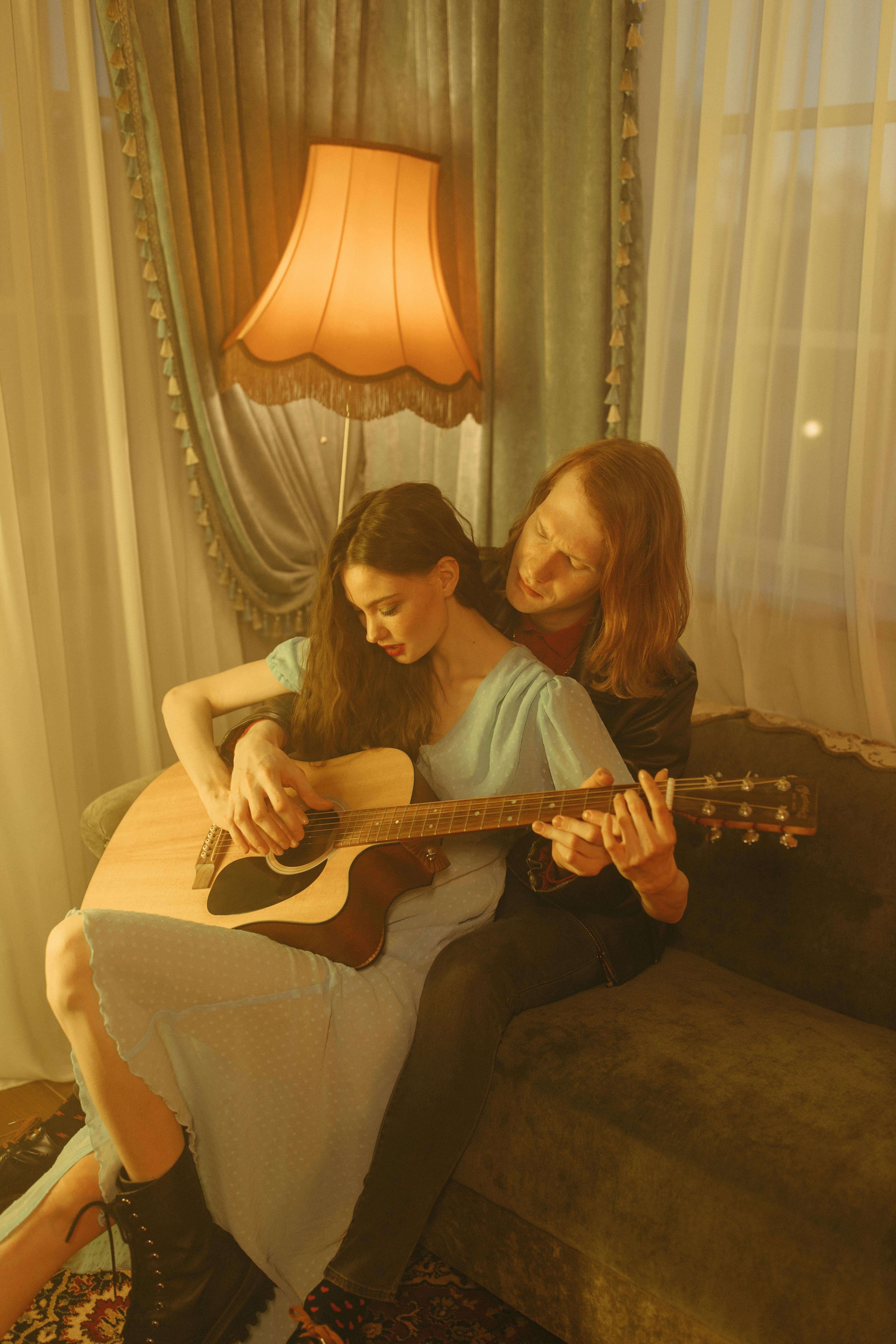 Romantic couple sitting together, sharing a guitar moment in a warm, inviting room.