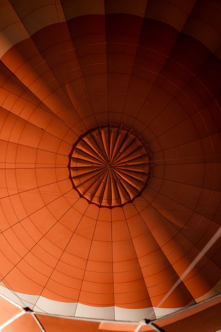 A detailed view of the orange canopy of a hot air balloon from inside looking upwards.