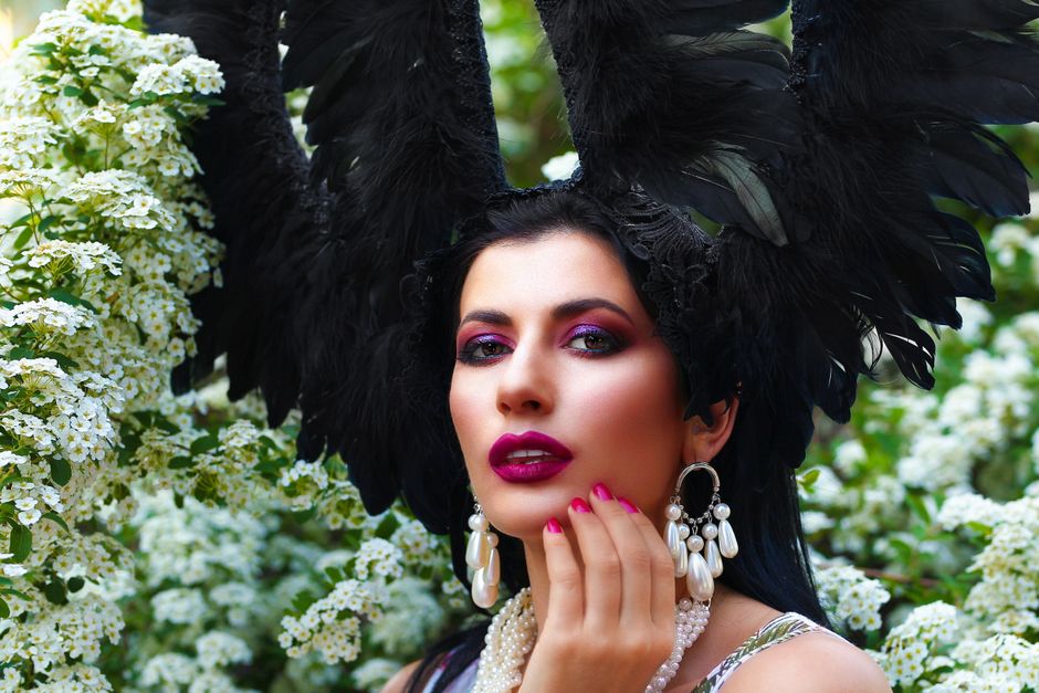 Captivating portrait featuring a woman with an elaborate feathered headdress amidst lush white blossoms.