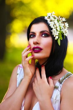 Striking portrait of a woman with bold makeup and floral hairpiece outdoors.