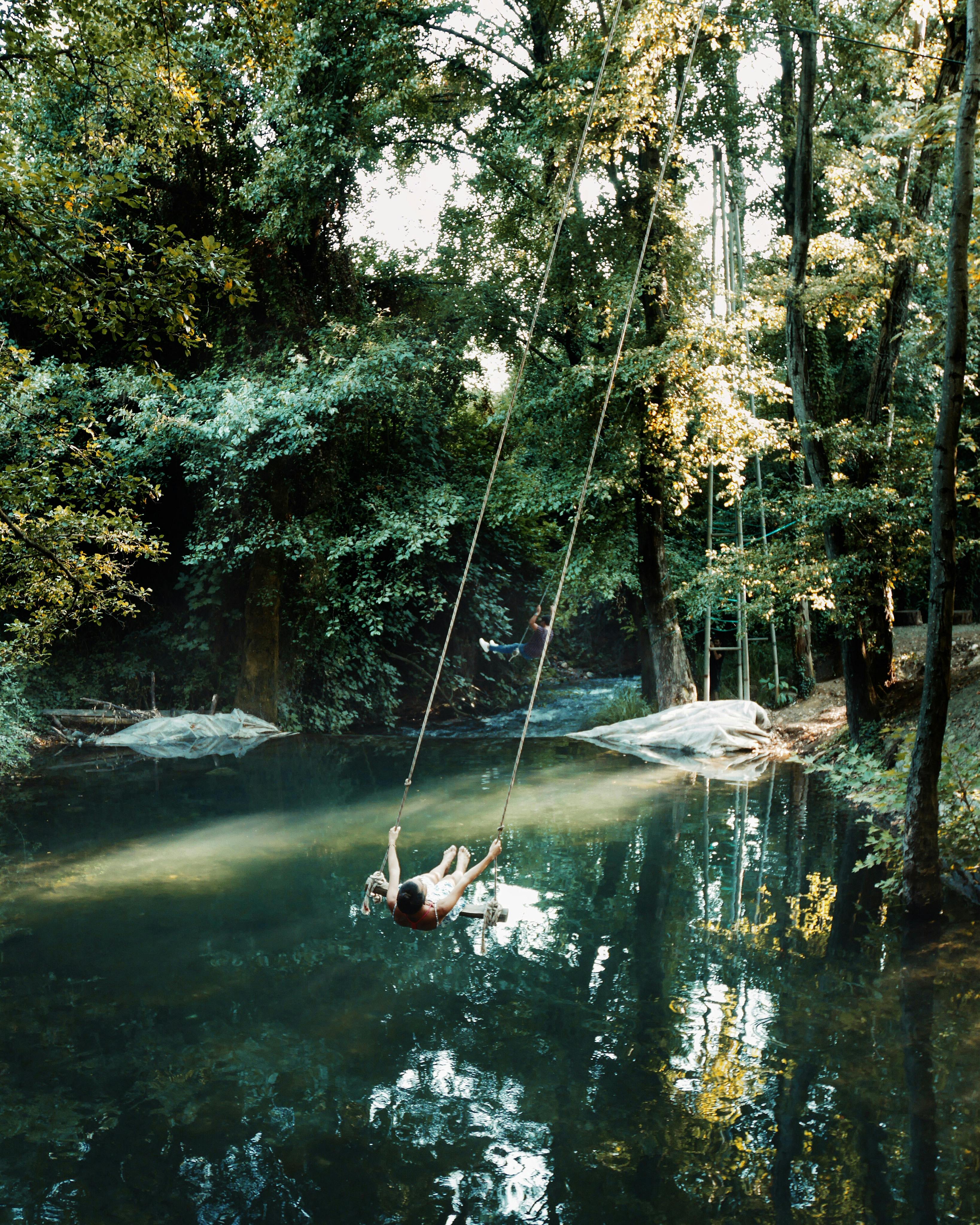 Free Man enjoying a swing over a tranquil forest pond in Muğla, Turkey during summer. Stock Photo