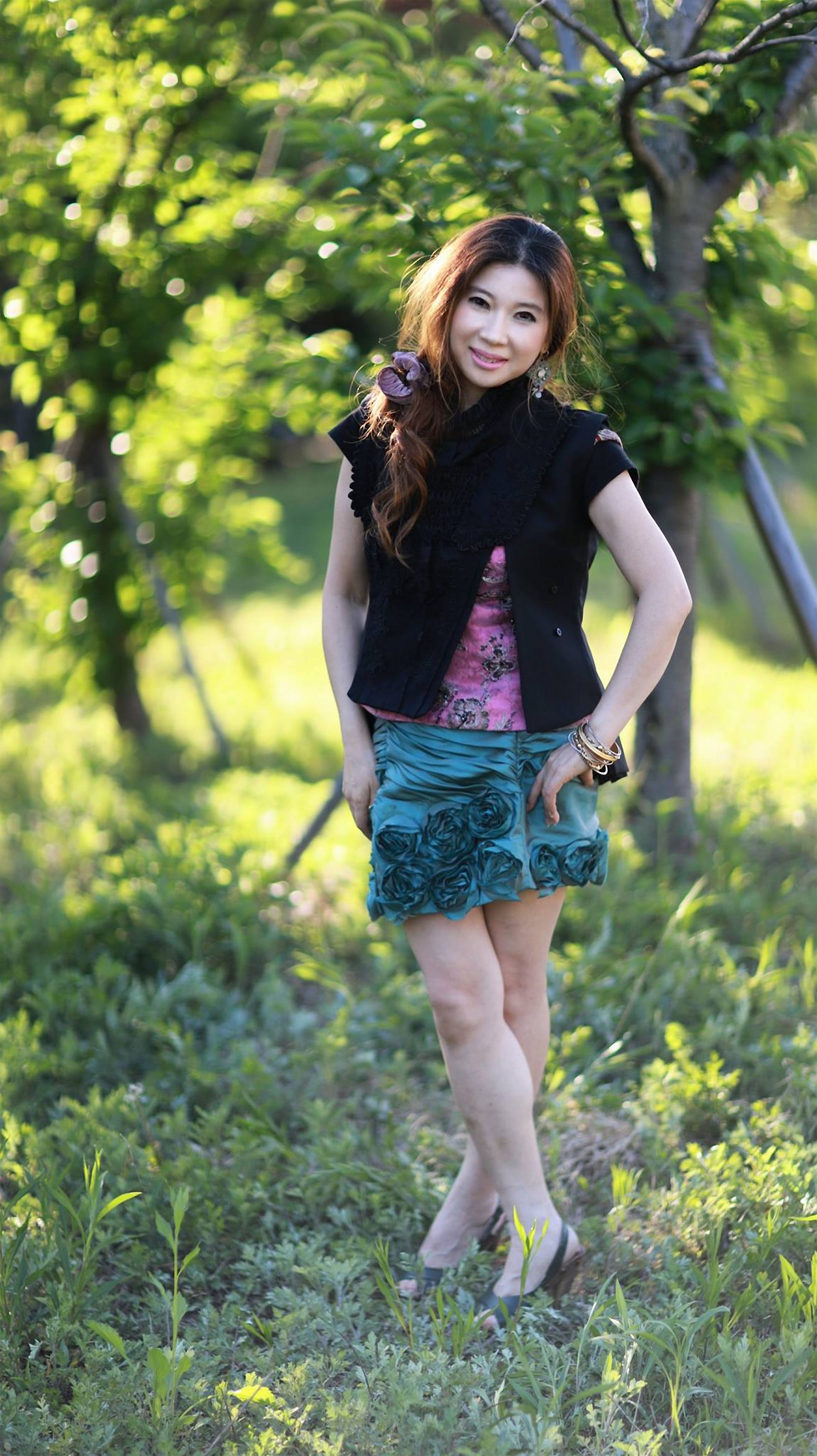 Fashionable woman posing outdoors in a colorful, stylish outfit amidst greenery.