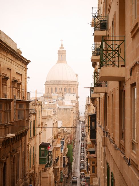 Charming street view in Valetta, Malta, featuring iconic architecture and a distant dome.