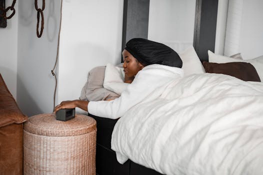 Woman in a black headscarf reaching for an alarm clock on a cozy morning.