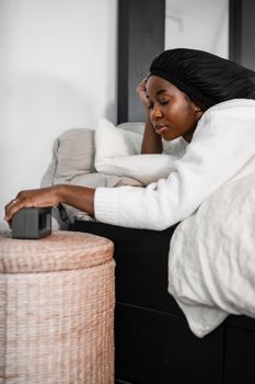 Woman in white sweater relaxing in bed, reaching for alarm clock on a peaceful morning.