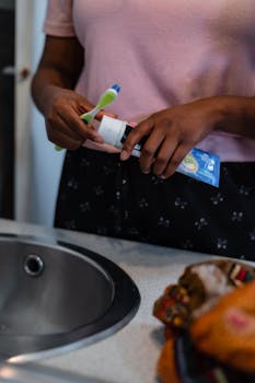 Close-up of a woman holding a toothbrush and toothpaste near a bathroom sink.