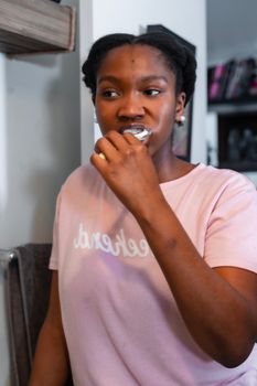 Black woman brushing teeth wearing a pink shirt, highlighting daily hygiene routine.