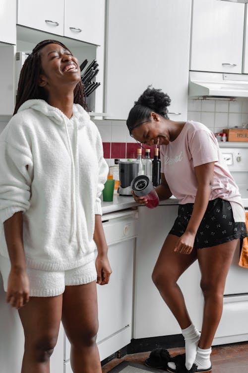 Free Women Laughing Together While in the Kitchen Stock Photo