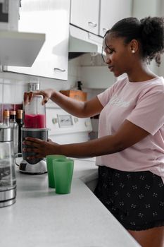African American woman preparing a fruit smoothie in a modern home kitchen.