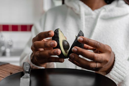 Close-up of hands preparing a fresh avocado in a kitchen setting.