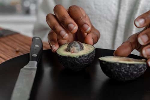 Free Hands slicing a fresh avocado on a black plate. Ideal for food blogs. Stock Photo